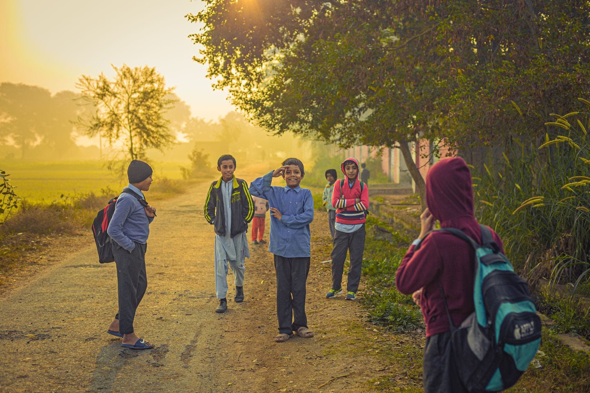 Children with school bags walking along a tree-lined path in early morning light