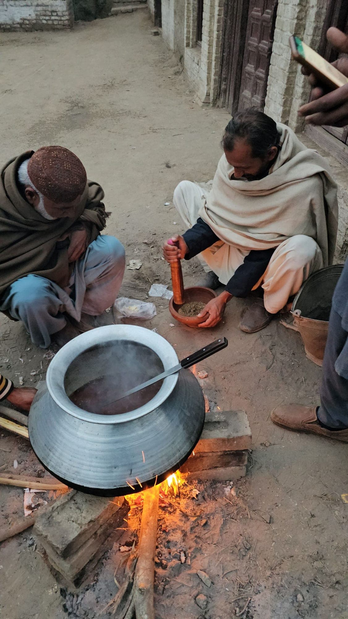 Men cooking a large pot of food over an open fire outdoors