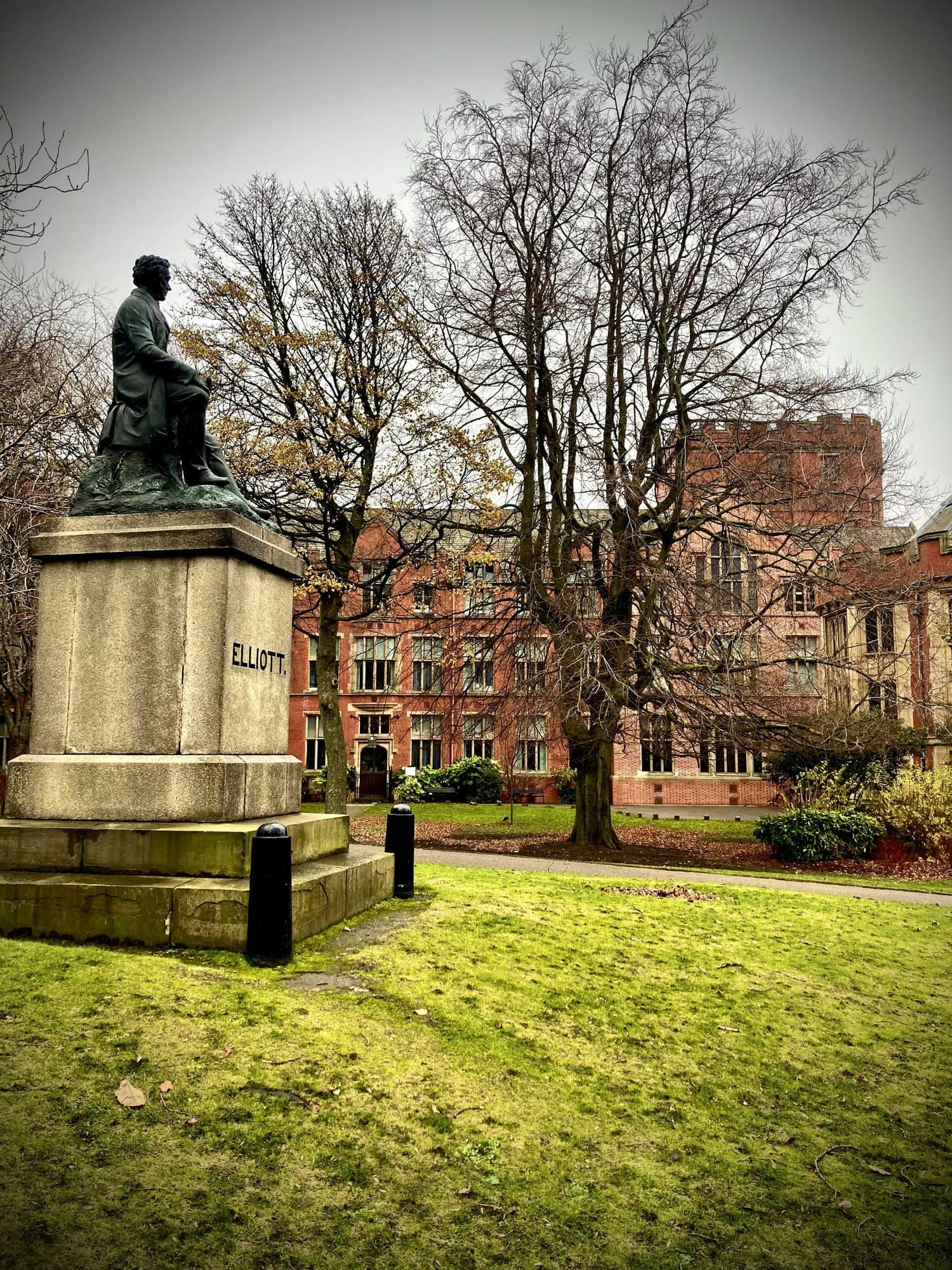 A statue in Weston Park in front of a red-brick university building in winter