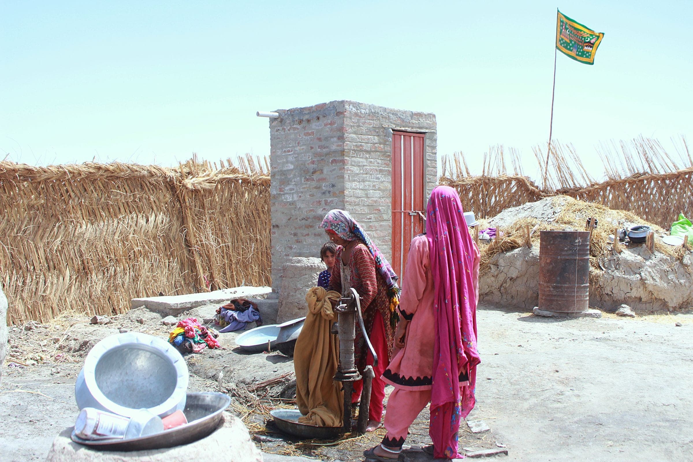 Women and a child drawing water from a hand pump beside their home in a village
