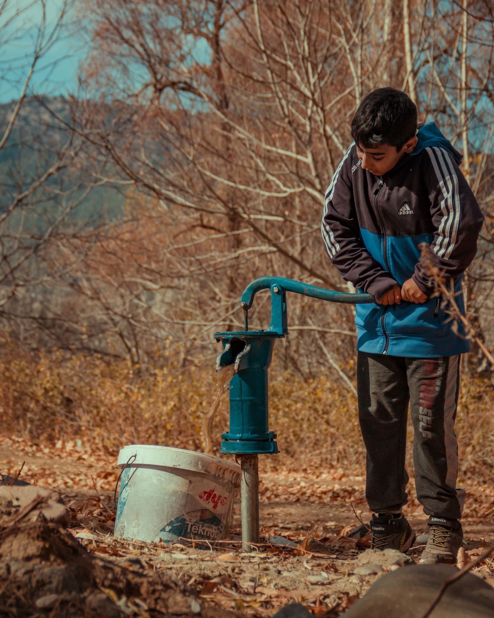 A boy pumping water from a green hand pump into a bucket