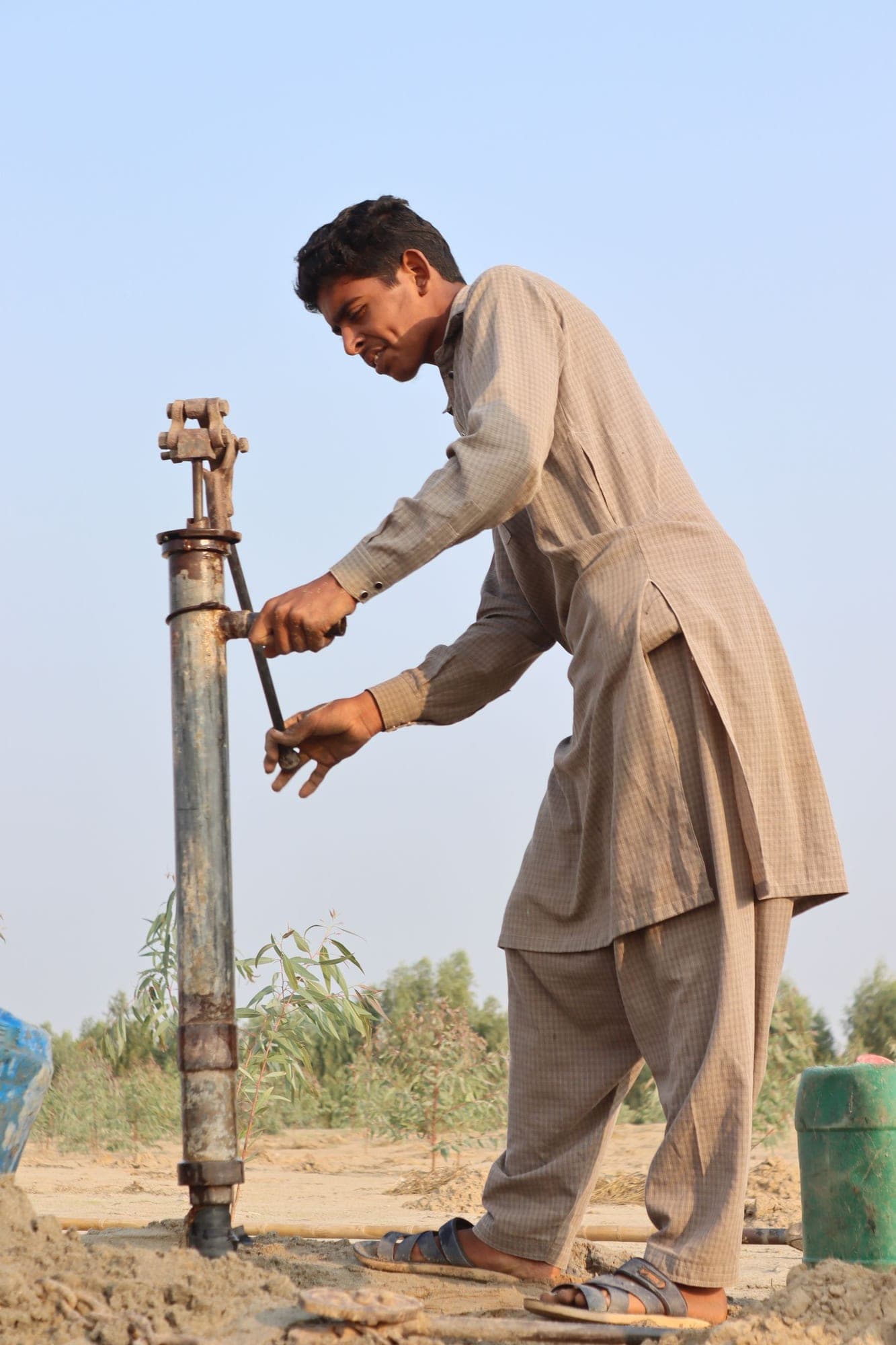 A man in shalwar kameez working the handle of a hand pump in a field