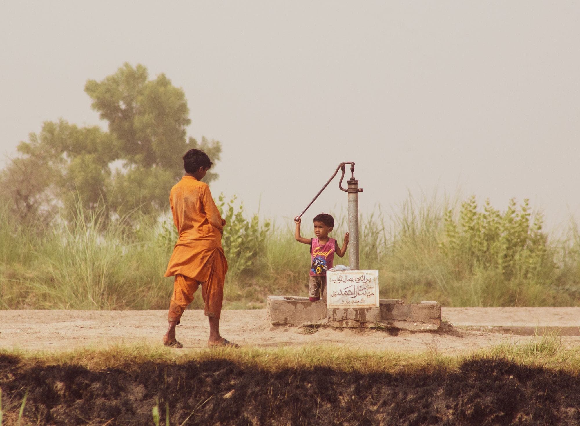 Two children working a hand pump in a hazy field